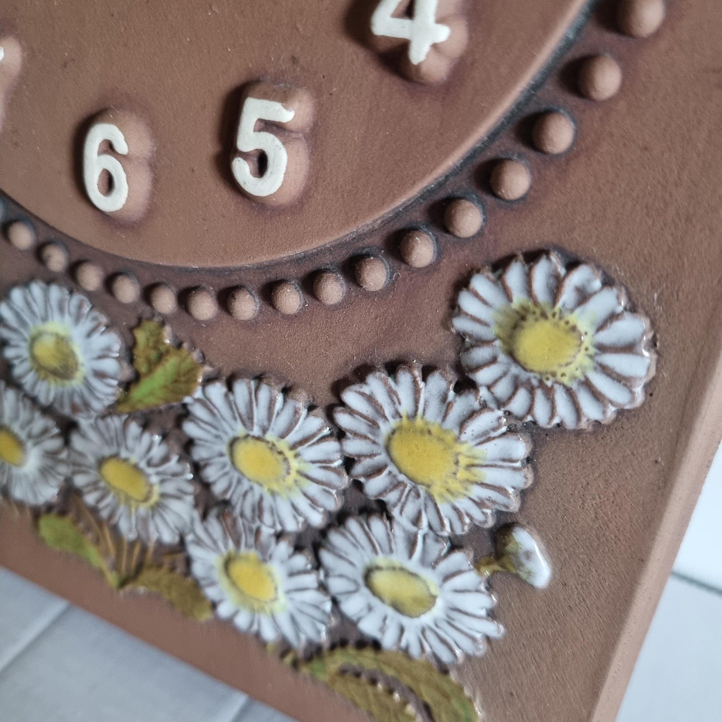 Close-up of JIE Keramik Gantofta Wall Clock – Prästkrage, Sweden 1970s with white daisies and yellow centers on brown ceramic surface.