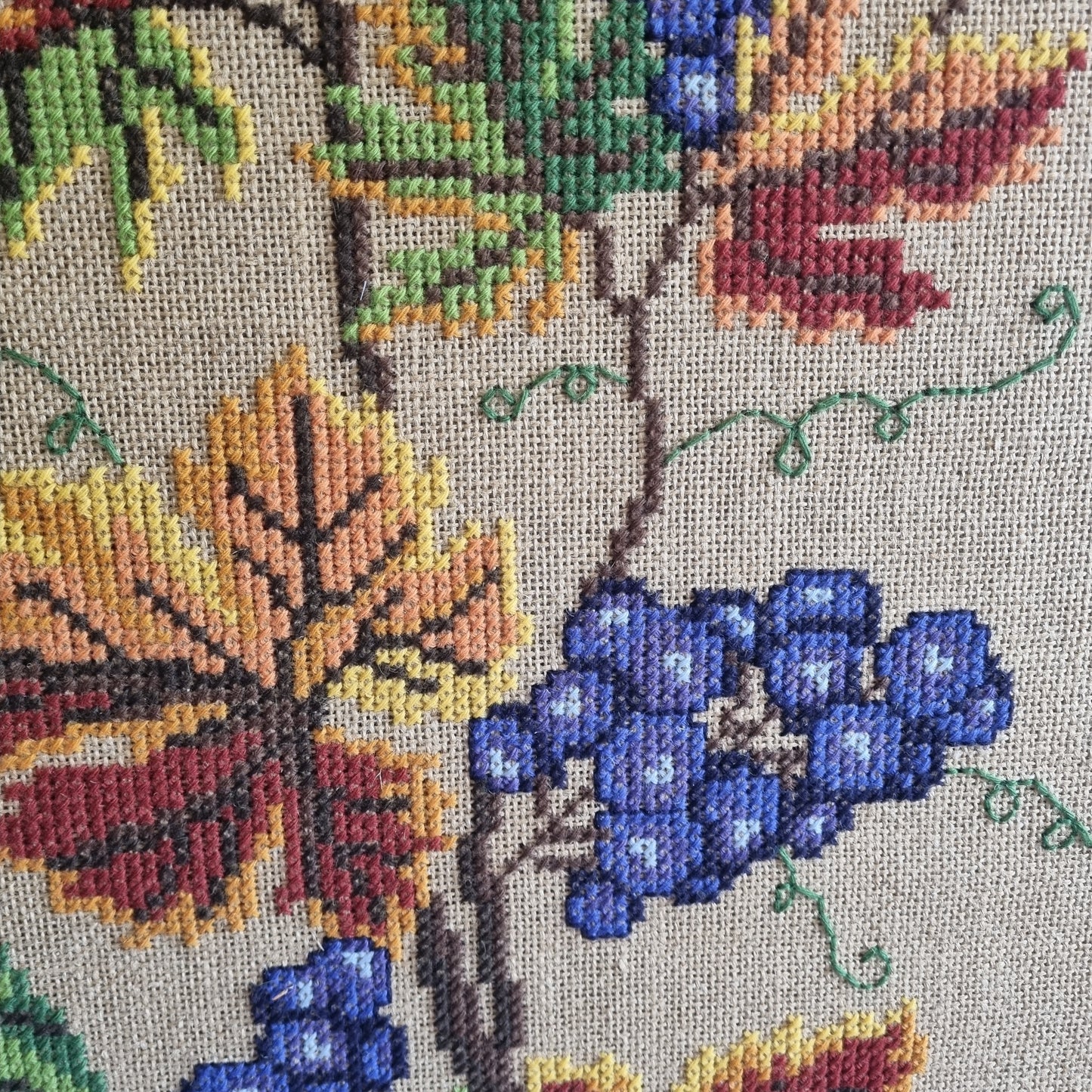 Detail of grapevine cross-stitch pattern, gold and rust autumn leaves on natural burlap