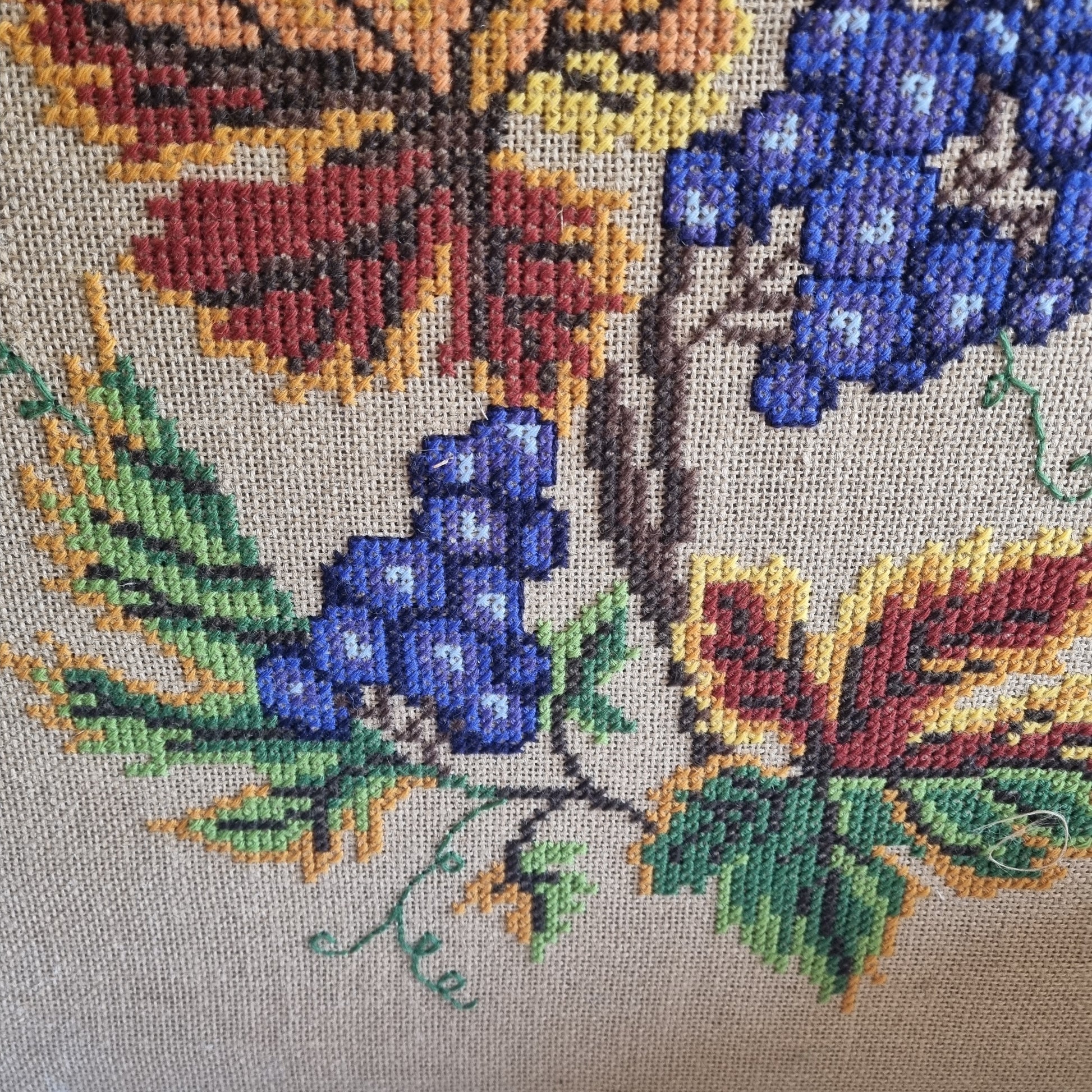 Detail of cobalt blue grapes and autumn leaves, cross-stitch embroidery on burlap