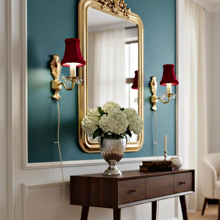 Vintage Rococo style gilded wall lamps pair with original velvet shades flanking an ornate gold mirror above a wooden console table.