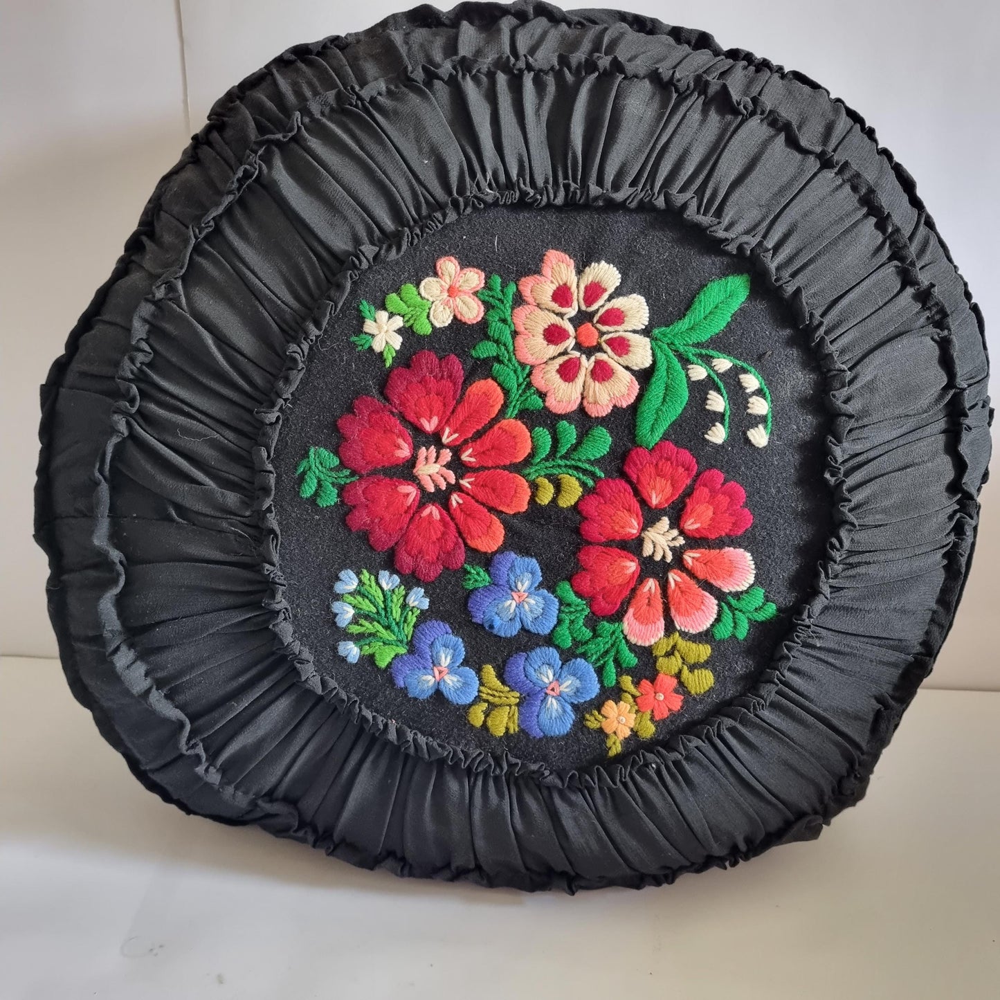 Vintage Embroidered Floral Throw Pillow: Black Ruffled Cushion with vibrant red, pink, and blue embroidered flowers on black fabric.